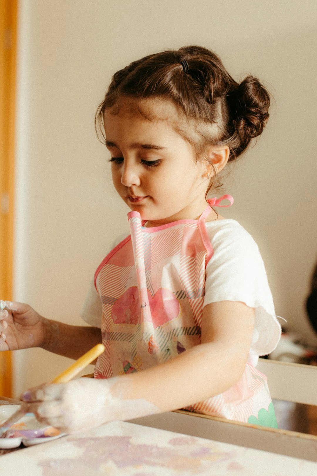 A young girl wearing an apron paints with a brush